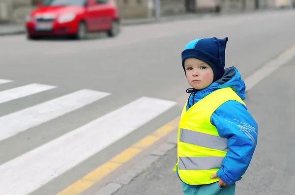 Mały chłopiec w kamizelce odblaskowej przed przejściem dla pieszych. — Zdjęcie stockowe