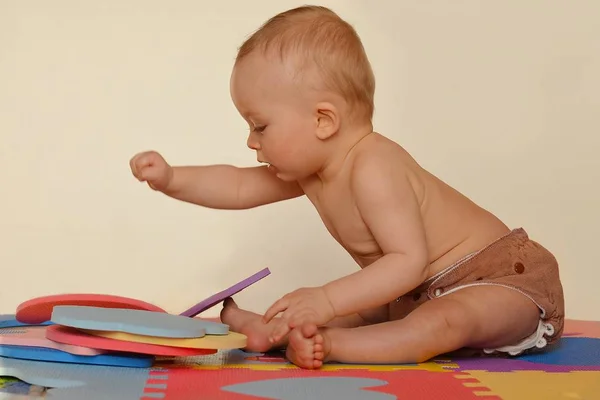 Lindo niño jugando con rompecabezas de espuma y sentado en las esteras de colores . — Foto de Stock