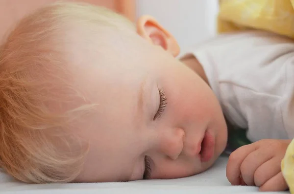 Блондинка хлопчик солодко спить у ліжку, покритому ковдрою . — стокове фото