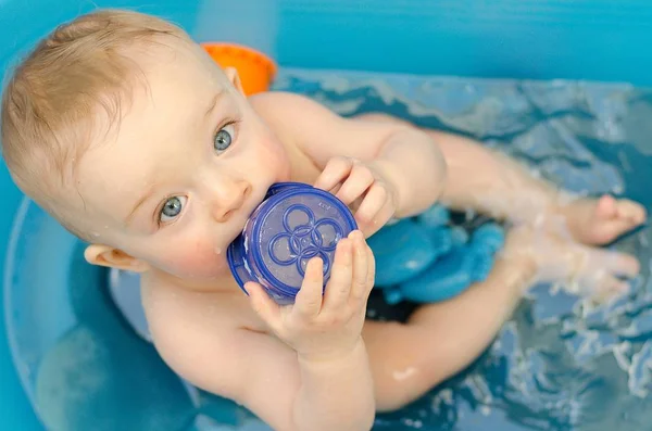 Lindo bebé bañándose en un tubo y jugando con tapas de plástico . — Foto de Stock