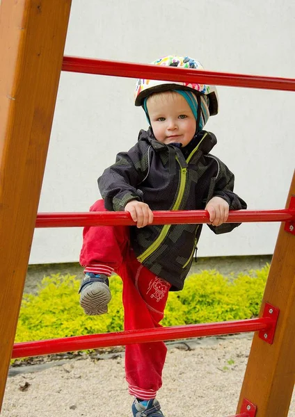 Mały chłopiec wspinający się na zjeżdżalnię na placu zabaw. — Zdjęcie stockowe
