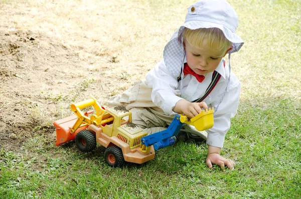 Dobrze ubrane dziecko (uczestnik wesela) bawi się koparką na trawie. — Zdjęcie stockowe