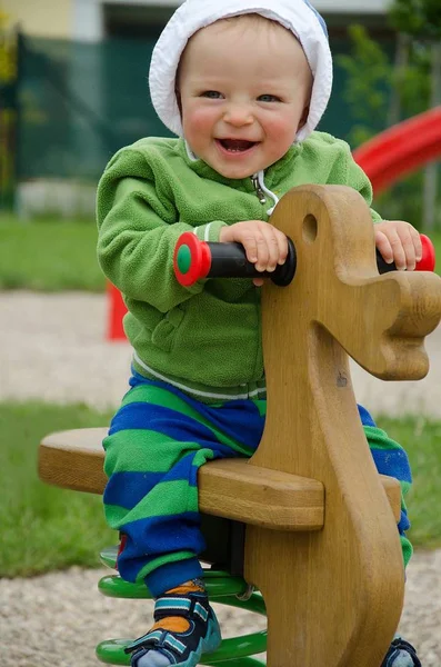 Portret szczęśliwego chłopca skaczącego na drewnianym koniu na placu zabaw. — Zdjęcie stockowe