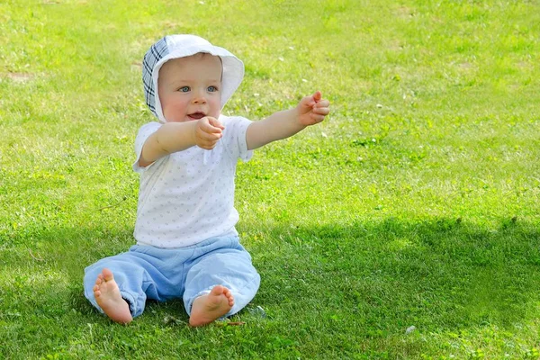 Cute toddler sitting alone in the shade of tree during sunny day in the nature. 스톡 사진