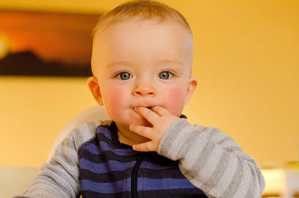 可愛いです赤ちゃん男の子でストライプシャツあります座っていると彼の指を吸います. — ストック写真