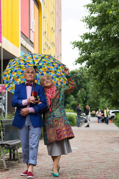 Elegantemente vestida pareja de ancianos caminando bajo un paraguas . — Foto de Stock