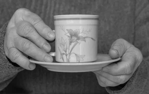 Tasse und Untertasse in den Händen einer alten Frau. — Stockfoto