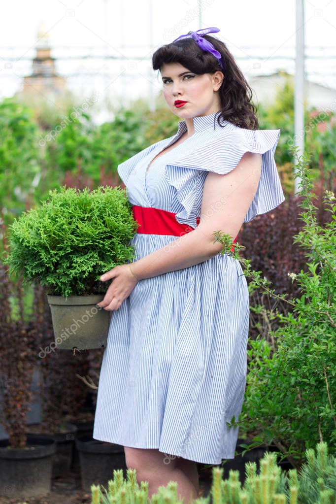 plus size Girl keeps pot with plant  in greenhouse