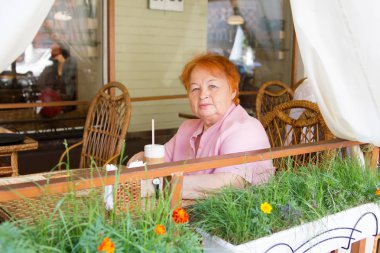 Elderly woman sitting in cafe in the afternoon. Summer. City. clipart