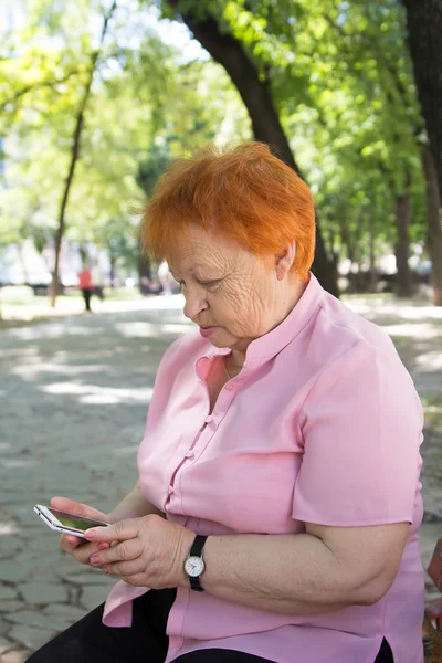 Elderly woman is calling by phone in the city park — Stock Photo, Image
