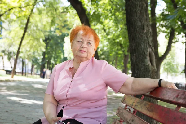 Пожилая женщина сидит на скамейке в городском парке — стоковое фото