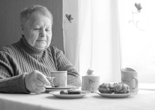 Пожилая женщина сидит за столом и пьет чай с пирожными . — стоковое фото