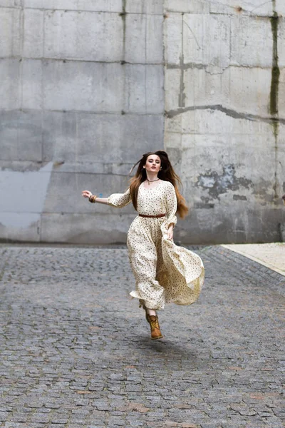 Dívka běží na ulici na pozadí šedé stěny. — Stock fotografie