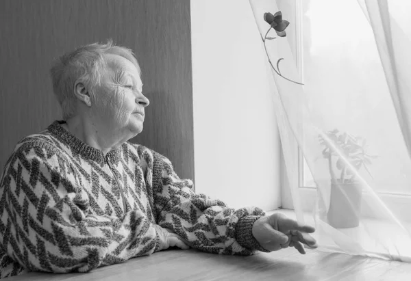 Donna anziana si siede e guarda fuori dalla finestra . — Foto Stock