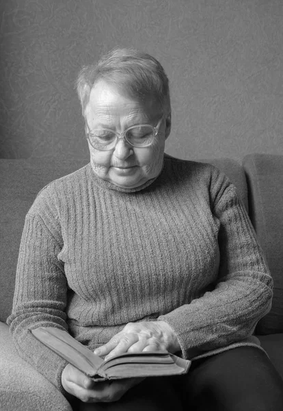 Femme âgée assise sur un canapé et lisant un livre . — Photo