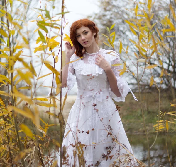Jovem mulher em vestido branco entre folhas amarelas no outono — Fotografia de Stock