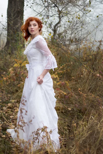 Леди с рыжими волосами в винтажном белом платье в лесу — стоковое фото