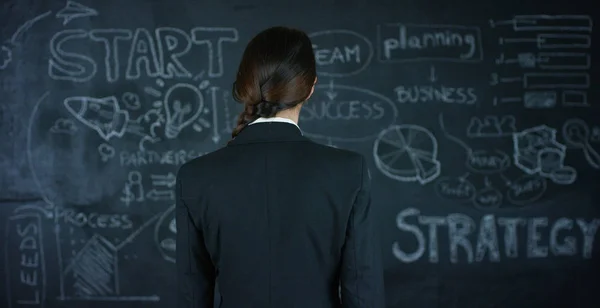美丽业务的女孩，一个营销的老师，在黑板上，在黑色的背景上绘制战略图。概念︰ 职业增长、 增长图表、 成功的女孩、 市场营销、 想法、 财政. — 图库照片