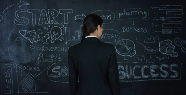 Die schöne BWL-Studentin, Marketinglehrerin, zeichnet eine Grafik des Erfolgs auf eine schwarze Tafel auf schwarzem Hintergrund. Konzept: Karrierewachstum, Wachstumschart, erfolgreiches Mädchen, Marketing, Ideen, Finanzen. — Stockfoto