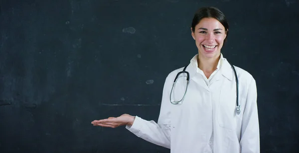 Portret van een mooie vrouwelijke arts (student) staat door een zwart bord, op een zwarte achtergrond. Concept: ideeën, school, Universiteit, chemie, wetenschap, leraren, geheugen, biologie, arts, college. — Stockfoto