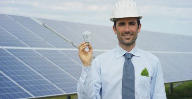 Technical expert in solar photovoltaic panels, remote control performs routine actions to monitor the system using clean renewable energy in the hand a light bulb. Concept of remote support technology clipart