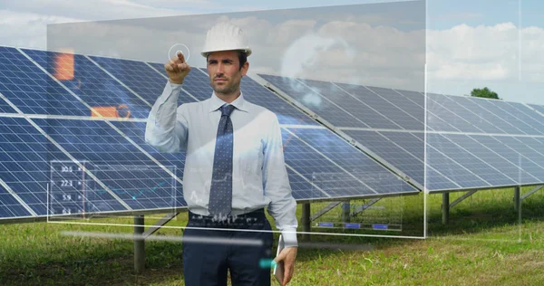 Un futuristico ingegnere-esperto in pannelli fotovoltaici solari, utilizza un ologramma con telecomando, compie azioni complesse per monitorare il sistema utilizzando tecnologie di supporto remoto per energie rinnovabili pulite — Foto Stock