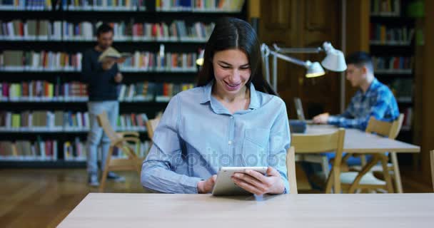 Porträtt av en vacker ung kvinna som ler lyckligt i ett bibliotek som håller böcker efter att söka och studera. Koncept: pedagogiska, porträtt, bibliotek, och flitig. — Stockvideo