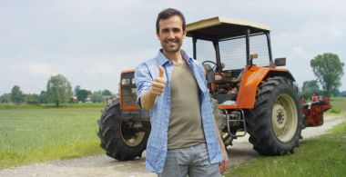 Bir gömlek içinde duran ve bir traktör ve doğa arka planda kameraya gülümseyen yakışıklı genç bir çiftçi portresi. Konsept: biyo ekoloji, temiz ortam, güzel ve sağlıklı insanlar, çiftçiler.