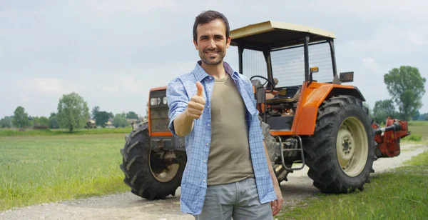 Retrato de um jovem fazendeiro bonito de pé em uma camisa e sorrindo para a câmera, em um trator e fundo da natureza. Conceito: bioecologia, ambiente limpo, pessoas bonitas e saudáveis, agricultores . — Fotografia de Stock