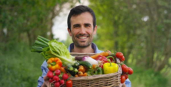 バスケットに新鮮な野菜を持って幸せな若い農夫の肖像画。自然生物、バイオ製品、バイオ エコロジー、健康的なサラダ、ベジタリアン自身の手によって成長の概念の背景に — ストック写真