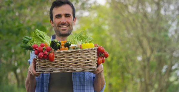 Portrait d'un jeune agriculteur heureux tenant des légumes frais dans un panier. Sur un fond de nature Le concept de produits biologiques, bio, bio écologie, cultivé par ses propres mains, végétariens, salades saines — Photo