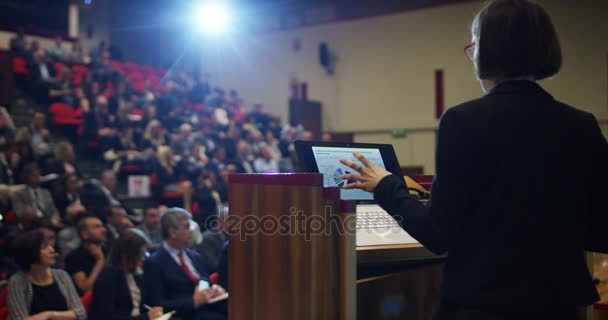 Uma mulher faz um discurso para o público em um auditório sobre uma convenção de economia e financiar seus negócios e aplaudir seu discurso — Vídeo de Stock