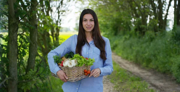 Hermosa joven sosteniendo una cesta de verduras, en el fondo de la naturaleza. Concepto: biología, bio-productos, bio-ecología, cultivar verduras, productos naturales puros y frescos, vegetarianos, saludables . — Foto de Stock