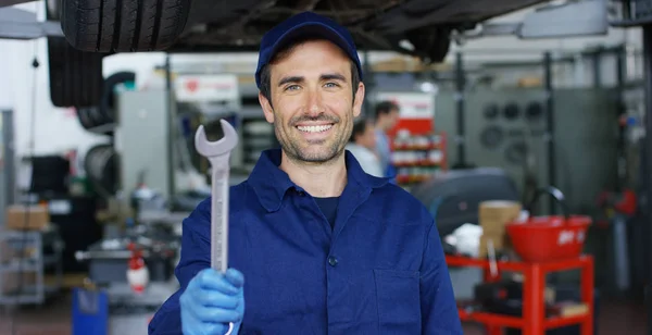 Retrato de um jovem mecânico de carro bonito em uma oficina de reparo de carro, mãos com uma chave inglesa. Conceito: reparação de máquinas, diagnóstico de falhas, especialista em reparação, manutenção técnica e computador de bordo . — Fotografia de Stock