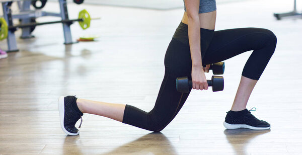 Young beautiful girl in the gym, squat with dumbbells, improving the muscles of the buttocks and legs. The concept: to love sports, to attend a gym, proper nutrition, a slender body, to be healthy.