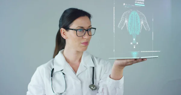 La doctora con bata blanca y estetoscopio, con tableta holográfica representaba el cuerpo del paciente, los pulmones del corazón, los músculos, los huesos. Concepto: Medicina futurista, asistencia mundial y el futuro . —  Fotos de Stock