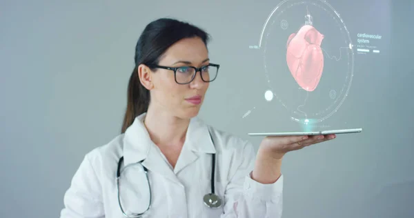 Γυναίκα γιατρός με άσπρο παλτό και στηθοσκόπιο, με ιδιόγραφη tablet εκπροσωπείται το σώμα του ασθενούς, την καρδιά τους πνεύμονες, τους μυς, οστά. Έννοια: Φουτουριστικό ιατρική, παγκόσμια βοήθεια και στο μέλλον. — Φωτογραφία Αρχείου