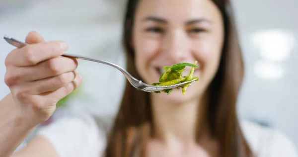 A beautiful woman lifts her fork with pasta al pesto, typical Italian dish, smiles and happy to eat healthy and tasty food. Concept: Italian spirit, food, healthy eating