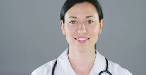 Porträtt av en kvinnlig läkare med vit päls och stetoskop leende tittar in kameran på vit bakgrund. Koncept: läkare, sjukvård, kärlek till medicin. — Stockfoto
