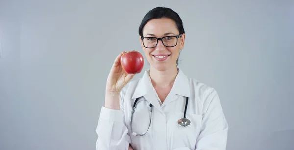 Retrato de un nutricionista, experto en alimentación y bienestar de la salud, sonríe mirando a la cámara y sosteniendo una manzana sobre un fondo blanco. Concepto: dieta, comida sana, saludable, peso saludable —  Fotos de Stock