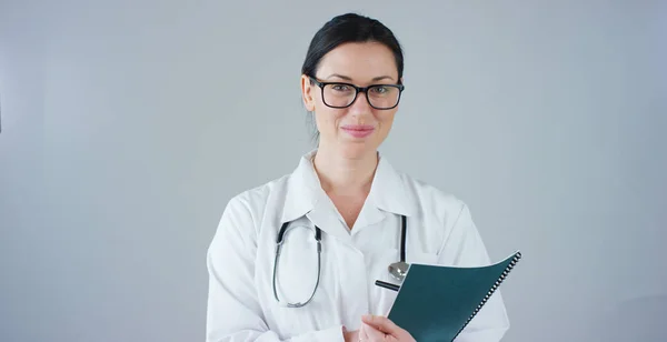 Retrato de uma médica com casaco branco e estetoscópio sorrindo olhando para a câmera no fundo branco. Conceito: médico, cuidados de saúde, amor pela medicina . — Fotografia de Stock