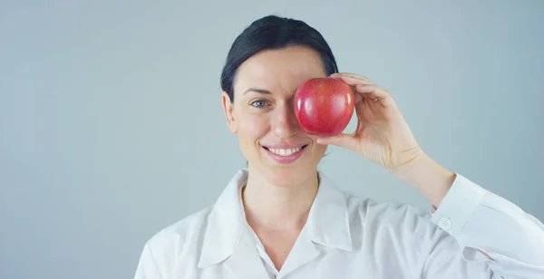 Porträtt av en nutritionist, expert på mat och hälsa-välfärd, ler tittar in i kameran och hålla ett äpple på en vit bakgrund. Koncept: kost, hälsosam, hälsokost, hälsosam vikt — Stockfoto