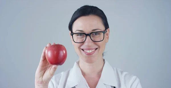 Potret seorang ahli gizi, seorang ahli kesejahteraan pangan dan kesehatan, tersenyum sambil melihat ke kamera dan memegang apel dengan latar belakang putih. Konsep: diet, sehat, makanan sehat, berat badan yang sehat — Stok Foto