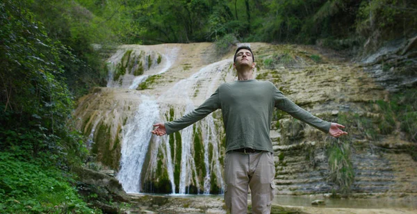 Pria muda yang bahagia, menghirup udara dalam dirinya sendiri untuk mengubah qi, merasa bebas dan mandiri, dengan latar belakang air terjun dan batu yang indah, konsep: alam, agama, bio, ekologi . — Stok Foto