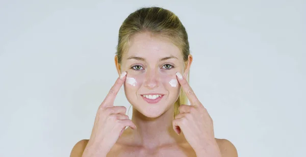 Portrait of a beautiful young girl smiling and looking at the camera, without makeup, smearing face of cream,on a white background.Concept:natural beauty,youth,skin care, always young,love yourself. — Stock Photo, Image