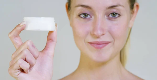 Portrait of a beautiful young girl smiling and looking at the camera, without makeup, holding cream, on a white background. Concept:natural beauty, youth, skin care, always young, love yourself. — Stock Photo, Image