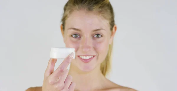 Retrato de uma linda menina sorrindo e olhando para a câmera, sem maquiagem, segurando creme, em um fundo branco. Conceito: beleza natural, juventude, cuidados com a pele, sempre jovem, amar a si mesmo . — Fotografia de Stock