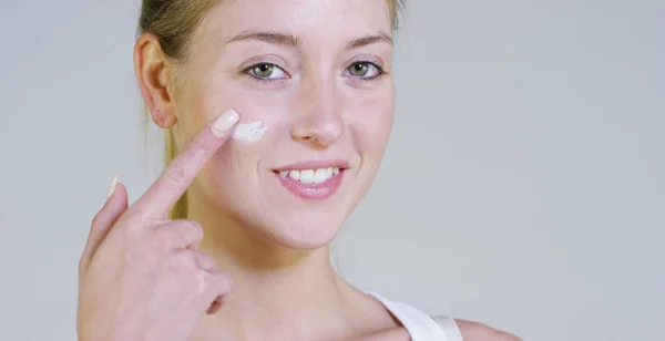 Portrait of a beautiful young girl smiling and looking at the camera, without makeup, smearing face of cream,on a white background.Concept:natural beauty,youth,skin care, always young,love yourself. — Stock Photo, Image