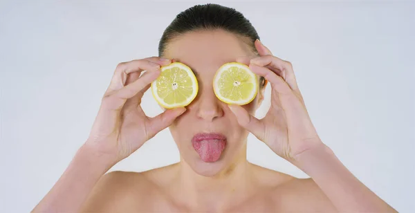 Портрет красивої молодої дівчини покриває очі лимоном і показує язик на білому тлі: Концепція: вітаміни, фрукти, свіжі, біологічні продукти, літо, весна, спа процедури, догляд за шкірою . — стокове фото