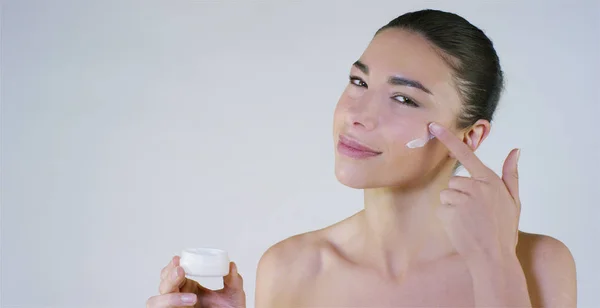 Retrato de una hermosa jovencita sonriendo y mirando a la cámara, sin maquillaje, manchando la cara de crema, sobre un fondo blanco.Concepto: belleza natural, juventud, cuidado de la piel, siempre joven, ámate . —  Fotos de Stock